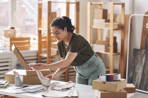 Jeune femme d'emballage nouveau chemisier en boîte à son lieu de travail travaillant dans la boutique en ligne