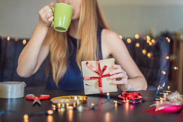 Une jeune femme emballe des cadeaux emballés dans du papier kraft avec un ruban rouge et or pour