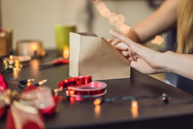 Une jeune femme emballe des cadeaux emballés dans du papier kraft avec un ruban rouge et or pour