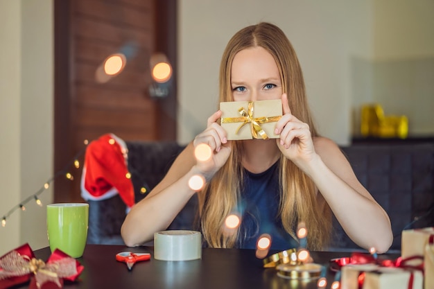 Une jeune femme emballe des cadeaux emballés dans du papier kraft avec un ruban rouge et or pour