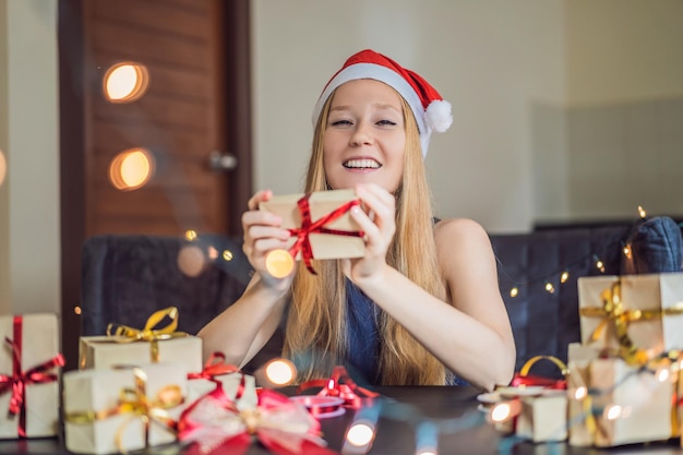 Une jeune femme emballe des cadeaux emballés dans du papier kraft avec un ruban rouge et or pour