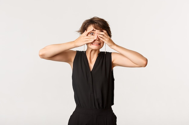 Une jeune femme embarrassée regardant entre les doigts quelque chose de très gênant.