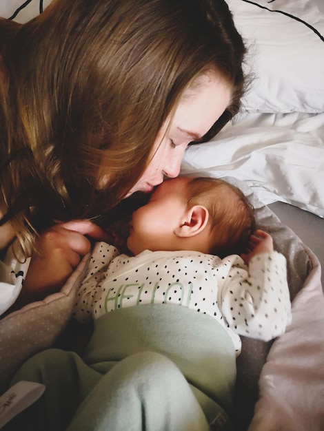 Une jeune femme embrasse un nouveau-né sur le lit à la maison.