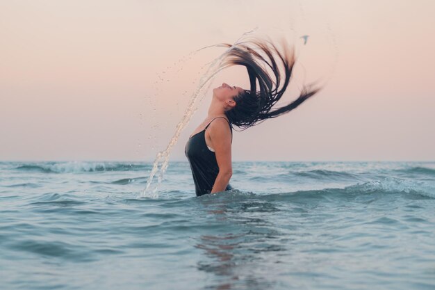 Une jeune femme émerge de la mer et forme une arche d'eau avec ses cheveux au coucher du soleil