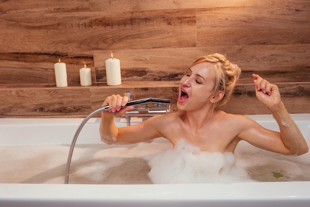 Jeune femme émotionnelle blonde se relaxant dans un bain avec de la mousse chantant fort