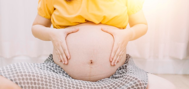 Jeune femme enceinte adulte en vêtements blancs touchant le gros ventre nu avec les mains montrant la forme Concept de grossesse Temps d'attente Gros plan isolé sur fond de mur gris clair