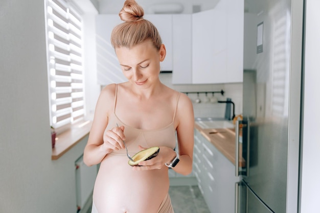 Une jeune femme enceinte d'apparence européenne dans sa cuisine avec un avocat dans les mains le concept d'une bonne nutrition des femmes enceintes pour le bon développement du fœtus