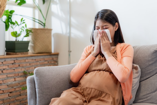 Jeune femme enceinte asiatique souffrant de grippe et d'éternuement, de nez qui coule, de nez bouché, puis de son coup de nez à l'aide d'un mouchoir