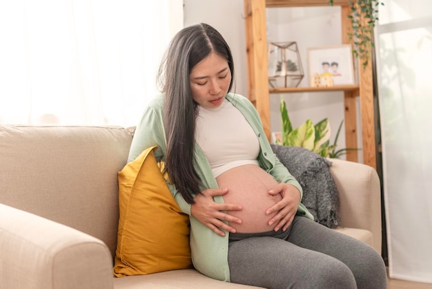 Jeune femme enceinte asiatique souffrant de maux de ventre assis sur un canapé dans le salon à la maison