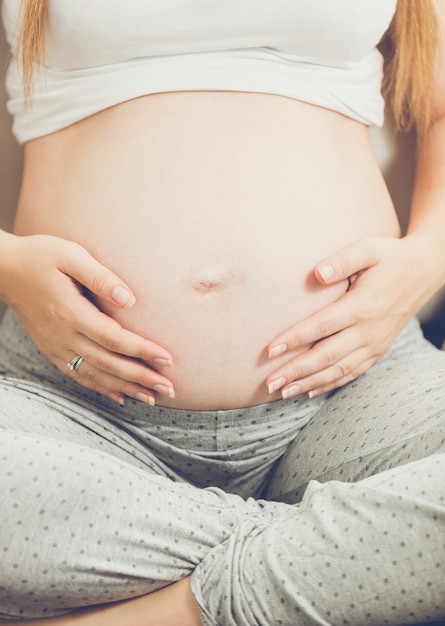 Photo jeune femme enceinte assise sur un canapé et se tenant la main sur le ventre