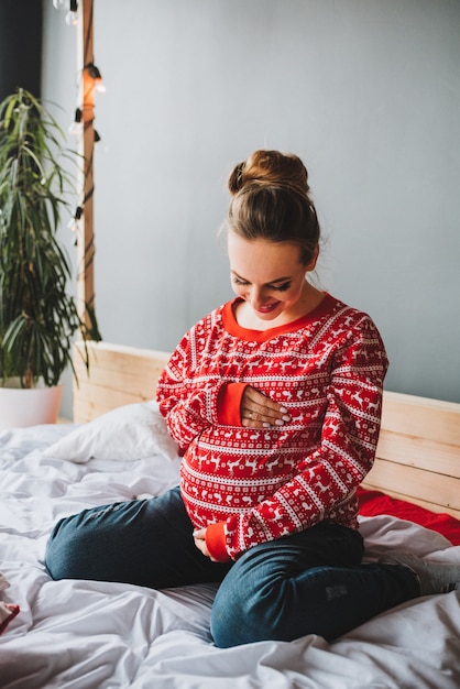 Jeune femme enceinte assise sur un lit regardant et tapotant son ventre