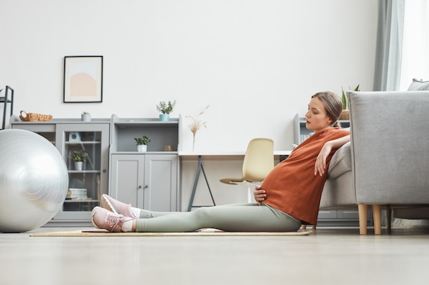 Jeune femme enceinte assise sur le sol et se reposant après un entraînement sportif dans la chambre