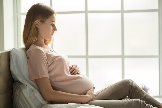 Jeune femme enceinte attend un bébé se reposant sur le lit à la maison touchant le ventre