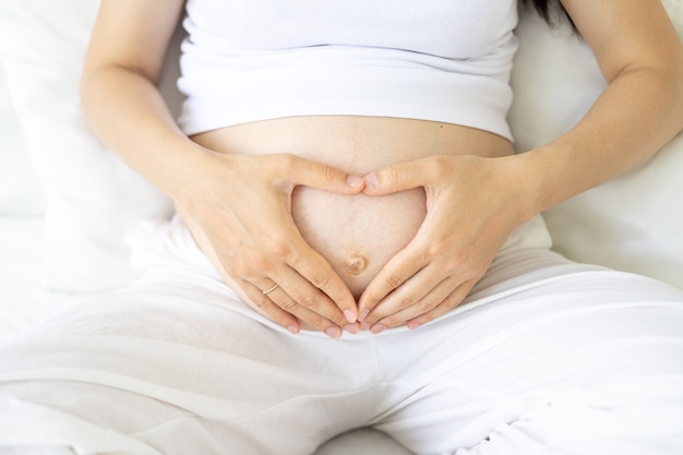 Une jeune femme enceinte en bonne santé à un stade avancé de la grossesse serre son ventre avec ses mains