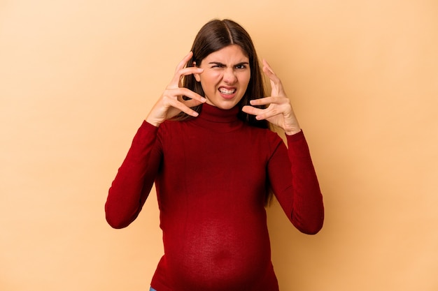 Jeune femme enceinte caucasienne isolée sur fond beige contrariée en criant avec les mains tendues.