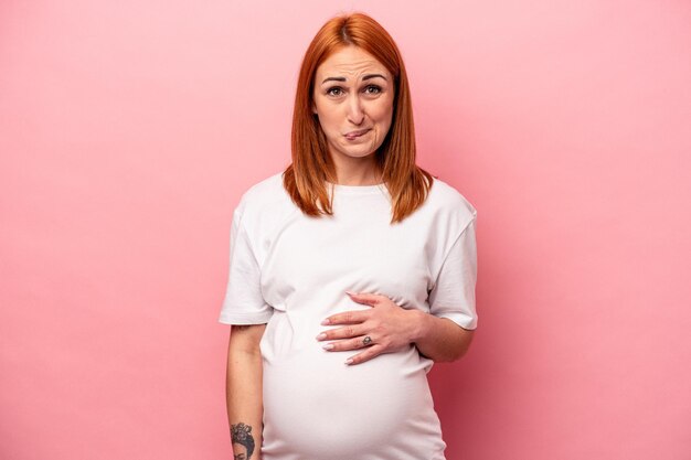 Jeune femme enceinte caucasienne isolée sur fond rose confus se sent douteux et incertain