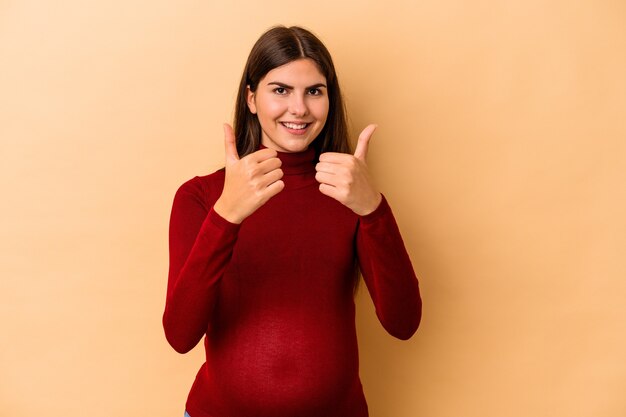 Jeune femme enceinte caucasienne isolée sur un mur beige avec des pouces vers le haut, des acclamations pour quelque chose, un soutien et un concept de respect.