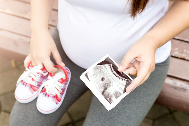 Jeune femme enceinte avec des chaussures de bébé en regardant rayons x dans le jardin