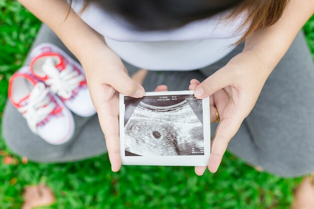 Jeune femme enceinte avec des chaussures de bébé en regardant rayons x dans le jardin