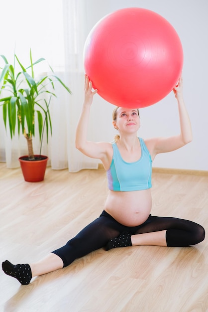 Photo jeune et femme enceinte en combinaison de sport faisant des exercices avec un gros ballon à la maison