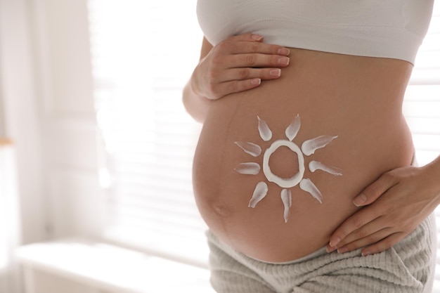 Jeune femme enceinte avec crème de protection solaire sur le ventre à l'intérieur agrandi Espace pour le texte