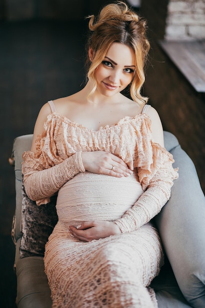 Une jeune femme enceinte dans une belle robe est assise à la fenêtre