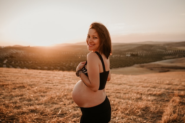 Jeune femme enceinte dans un champ de blé au coucher du soleil