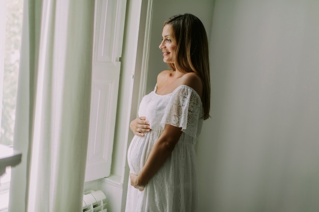 Jeune femme enceinte debout près de la fenêtre