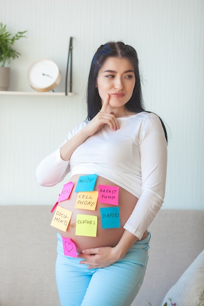 Jeune femme enceinte essayant de ne pas oublier des trucs à l'hôpital. Femme attendue avec des notes sur le ventre.