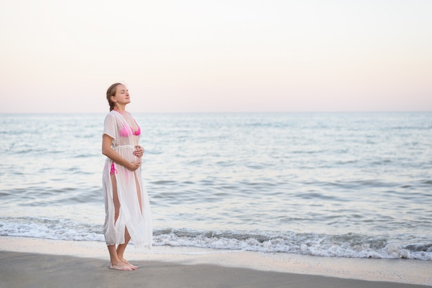 Jeune femme enceinte est debout au bord de la mer