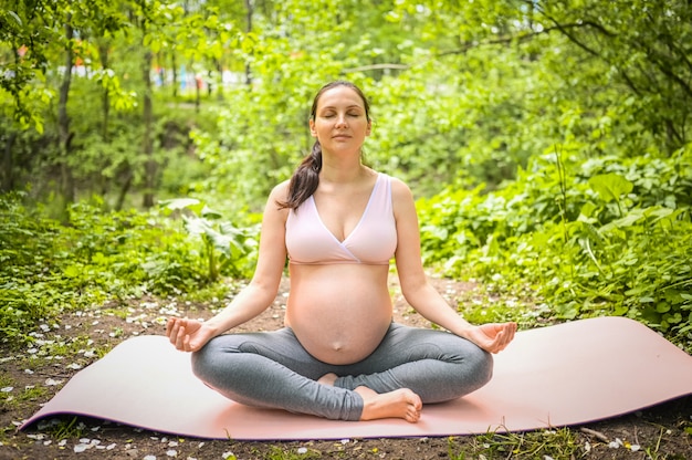 jeune femme enceinte, faire du yoga exerçant dans le parc en plein air