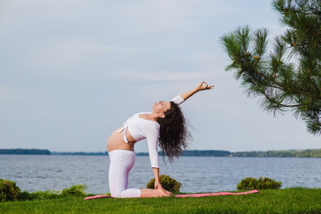 Jeune femme enceinte, faire du yoga en plein air