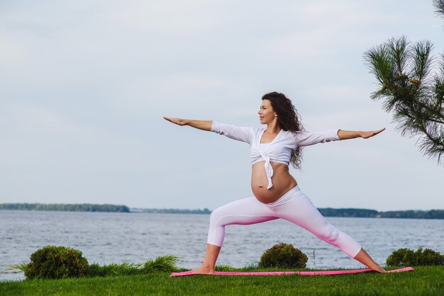 Jeune femme enceinte, faire du yoga en plein air