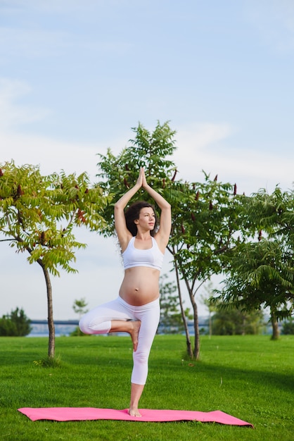 Jeune femme enceinte, faire du yoga en plein air