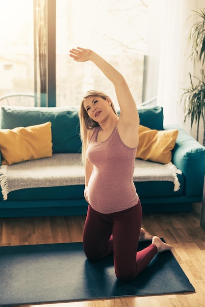 Jeune femme enceinte faisant de l'exercice à la maison le matin. Elle fait de l'exercice d'étirement.