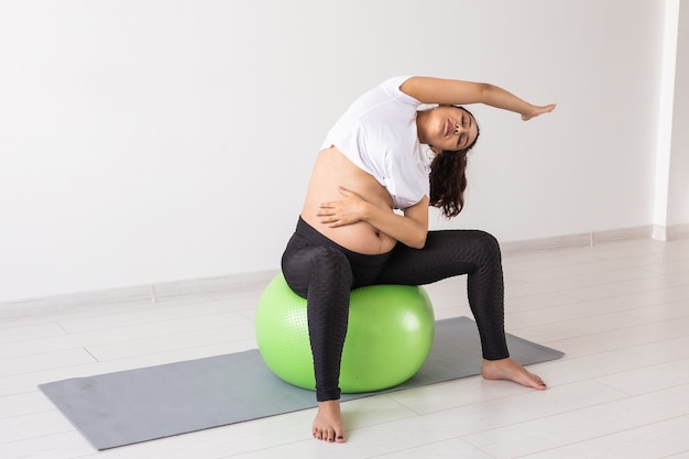 Jeune femme enceinte flexible, faire de la gymnastique avec ballon de fitness