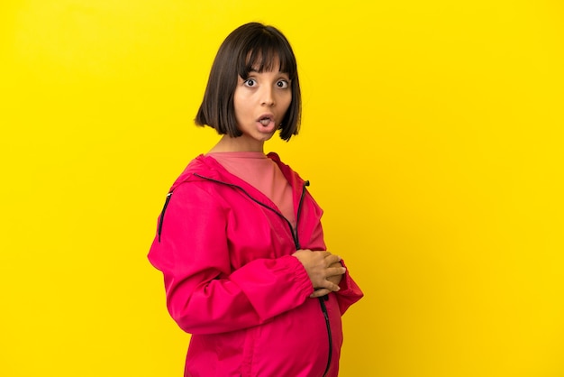 Jeune femme enceinte sur fond jaune isolé avec une expression faciale surprise