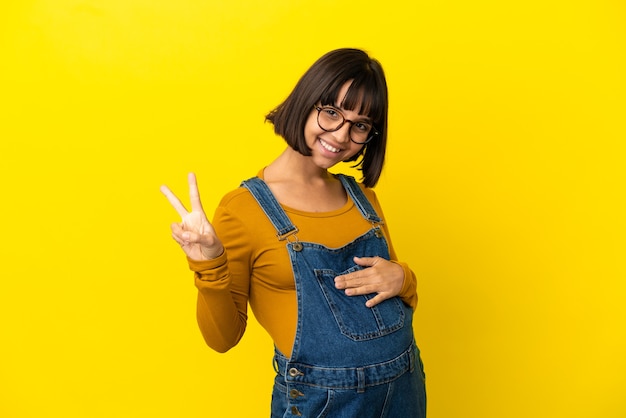 Jeune femme enceinte sur fond jaune isolé montrant le signe de la victoire avec les deux mains