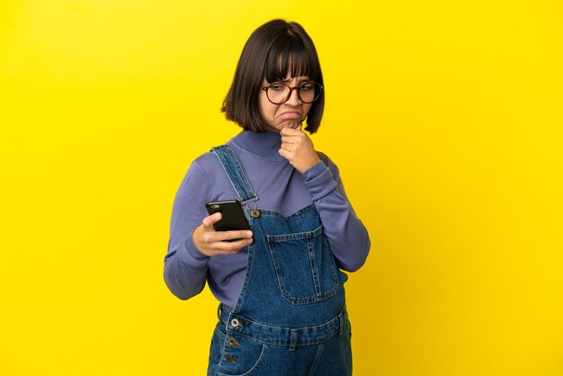 Jeune femme enceinte sur fond jaune isolé pensant et envoyant un message