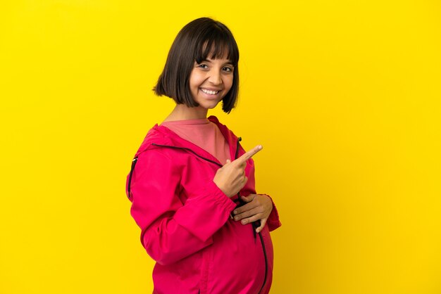 Jeune femme enceinte sur fond jaune isolé pointant sur le côté pour présenter un produit