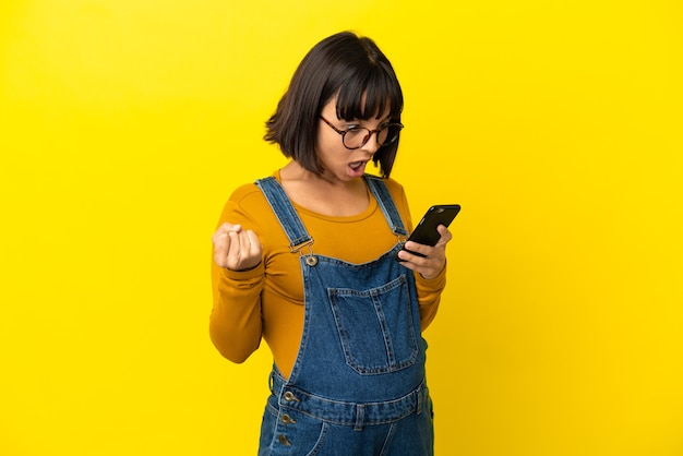 Jeune femme enceinte sur fond jaune isolé surpris et envoyant un message