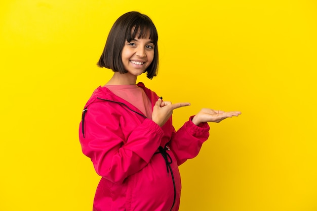 Jeune femme enceinte sur fond jaune isolé tenant un espace de copie imaginaire sur la paume pour insérer une annonce