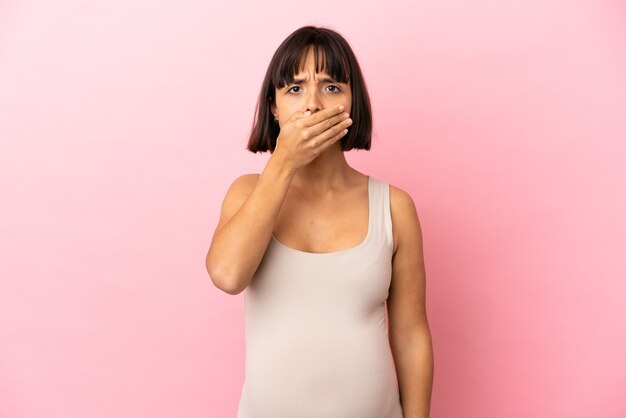 Jeune femme enceinte sur fond rose isolé couvrant la bouche avec la main