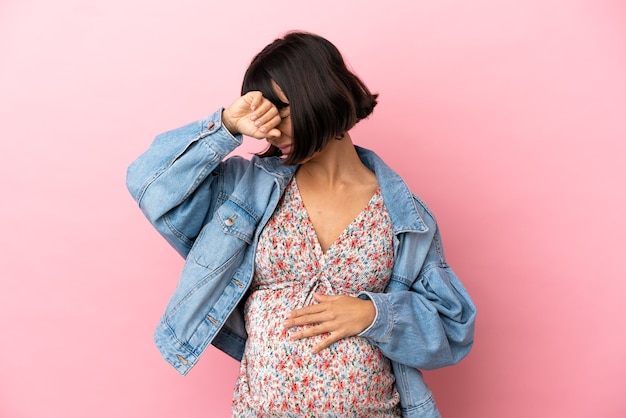 Jeune femme enceinte sur fond rose isolé couvrant les yeux par les mains