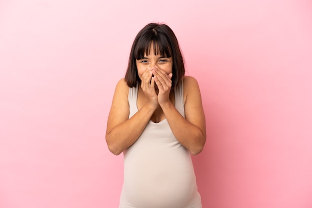 Jeune femme enceinte sur fond rose isolé heureux et souriant couvrant la bouche avec les mains