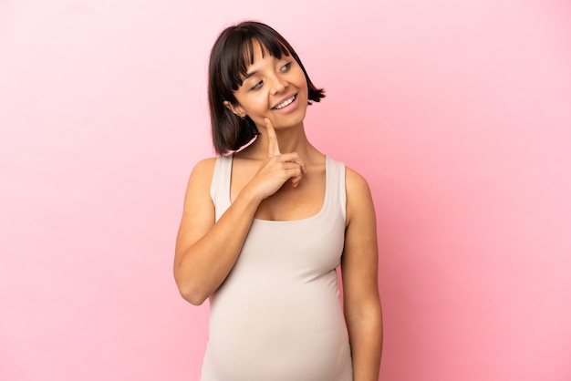 Jeune femme enceinte sur fond rose isolé en pensant à une idée tout en levant les yeux