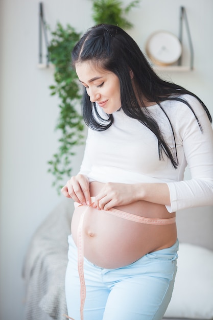 Jeune femme enceinte à l'intérieur. Dame mesurant son stomack rond. Belle femme attend bébé.