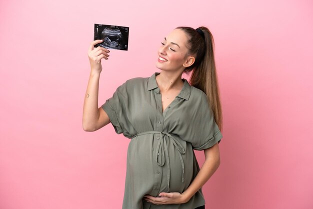 Jeune femme enceinte isolée sur fond rose et tenant une échographie