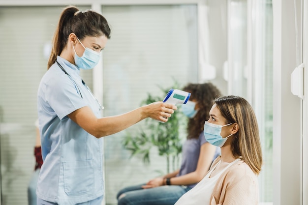 Jeune femme enceinte avec un masque facial dont la température est vérifiée avant le vaccin contre le coronavirus.