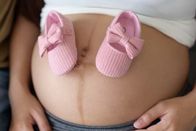 Jeune femme enceinte mettant des chaussures de bébé sur le ventre famille et concept de soins de grossesse